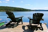 stock photo of blue sky  - Two adirondack wooden chairs on dock facing a blue lake with clouds reflections - JPG 
