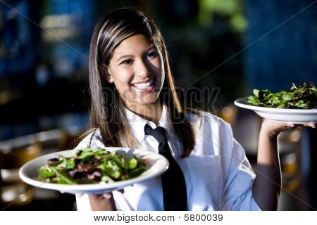 Picture or Photo of Hispanic waitress serving two plates of salad in a restaurant
