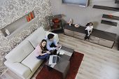 stock photo of finance  - young happy family at bright and modern living room puting money in piggy bank and working on laptop computer on home finance - JPG 