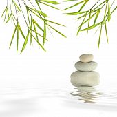 stock photo of zen  - Zen abstract of gray spa stones in perfect balance and bamboo leaf grass with reflection over rippled water against a white background - JPG 
