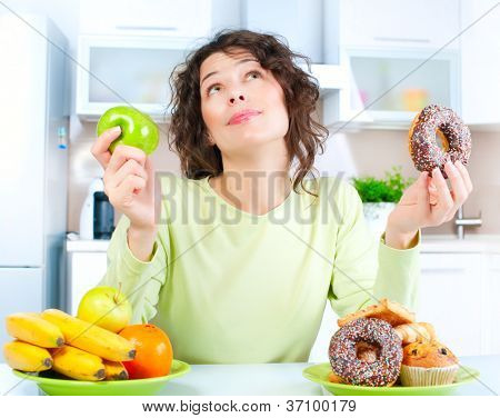 Picture or Photo of Diet. Dieting concept. Healthy Food. Beautiful Young Woman choosing between Fruits and Sweets
