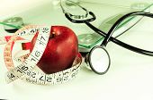 image of health  - red apple wrapped with tape measure near scale with stethoscope - JPG 