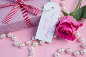 stock photo of wrapped  - Pink rose with gift and string of pearls and tag for mothers day on pink surface - JPG 