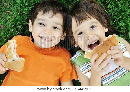 Picture or Photo of Two cute boys laying on ground in nature and happily eating healthy food