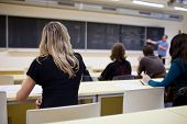 stock photo of college  - young pretty female college student sitting in a classroom full of students during class  - JPG 