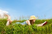 image of blue sky  - Young teenage girl reading book in summer meadow with straw hat - JPG 