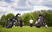 stock photo of golf  - Two golf bags standing in front of a group of golf players putting on green - JPG 
