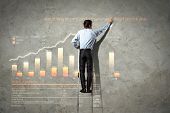 stock photo of leadership  - businessman standing on ladder drawing diagrams and graphs - JPG 