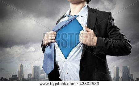 Picture or Photo of Image of young businessman showing superhero suit underneath his shirt standing against city background