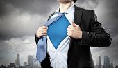 stock photo of standing  - Image of young businessman showing superhero suit underneath his shirt standing against city background - JPG 