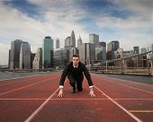 foto of competition  - Businessman kneeling on the starting grid of a running track with cityscape on the background - JPG 