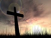 picture of religion  - Concept conceptual black cross or religion symbol silhouette in grass over a sunset or sunrise sky with sunlight clouds background - JPG 