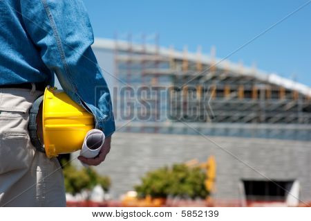 Picture or Photo of A construction worker or foreman at a construction site with blue prints and a hard hat