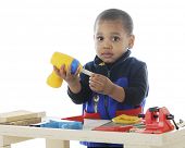 foto of toddlers  - Closeup image of an adorable toddler playing carpenter with plastic tools on a work bench - JPG 
