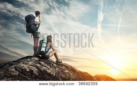 Picture or Photo of Two tourists with backpacks enjoying sunset on top of a mountain
