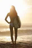 foto of beach  - Rear view of beautiful sexy young woman surfer girl in bikini with white surfboard on a beach at sunset or sunrise - JPG 