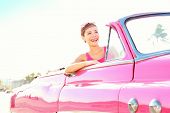 image of multiracial  - Retro woman smiling happy in old pink vintage car driving on road trip on beautiful summer day - JPG 