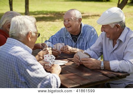 Picture or Photo of Active retirement old people and seniors free time group of four elderly men having fun and playing cards game at park. Waist up
